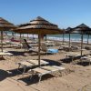 Spiaggia sabbiosa con lettini sotto ombrelloni di paglia e il mare sullo sfondo.