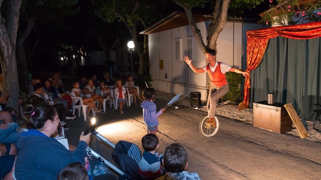 Spettacolo serale con artista su monociclo davanti a un pubblico di bambini.