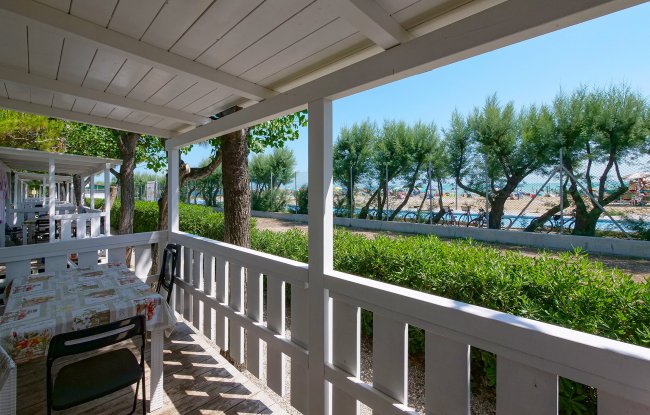Veranda coperta con tavolo e sedie, vista su alberi e mare.