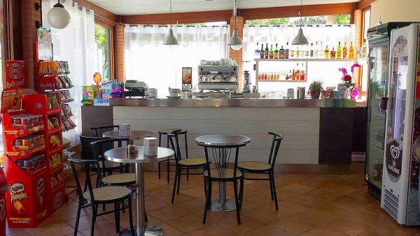 Interno di un bar con tavoli, sedie e scaffali di bevande e snack.