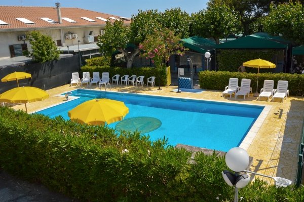 Piscina all'aperto con lettini e ombrelloni gialli, circondata da alberi e siepi.