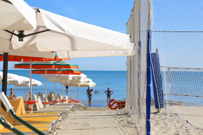 Spiaggia con ombrelloni e rete da beach volley vicino al mare.