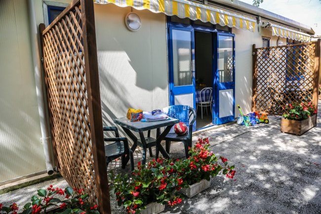 Un patio con tavolo, sedie, fiori e una tenda da sole a strisce gialle e bianche.
