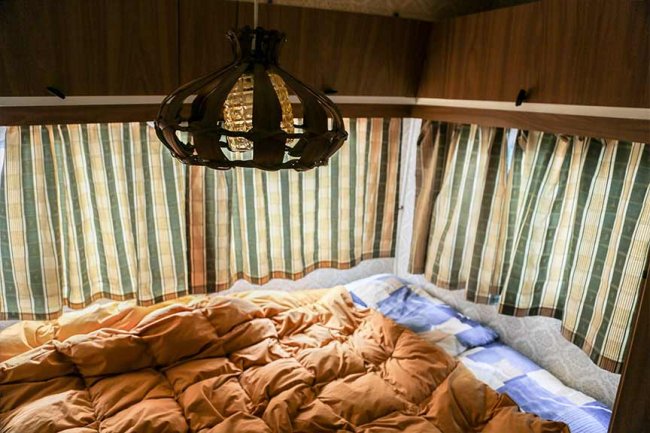 Interno di una roulotte con letto e lampadario.