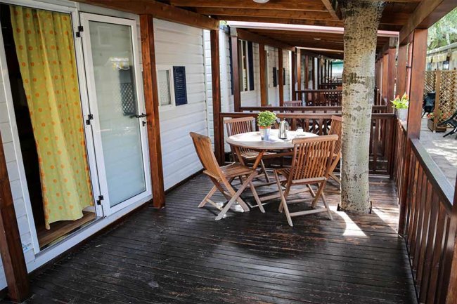 Terrazza in legno con tavolo rotondo e sedie, albero che attraversa il pavimento.