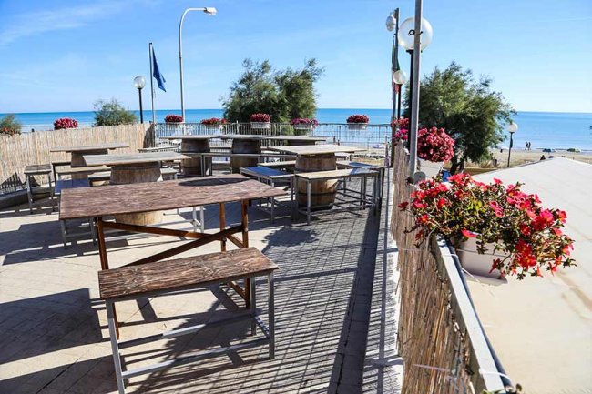 Terrazza con tavoli di legno e vista mare, decorata con fiori colorati.
