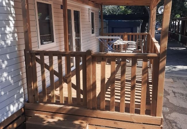Una veranda in legno con ringhiere e sedie sotto una copertura.