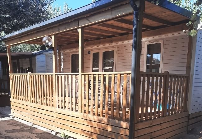 Una casa mobile con una veranda in legno ombreggiata e recintata.