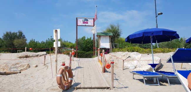 Passerella di legno conduce a una spiaggia con ombrelloni blu e sdraio.