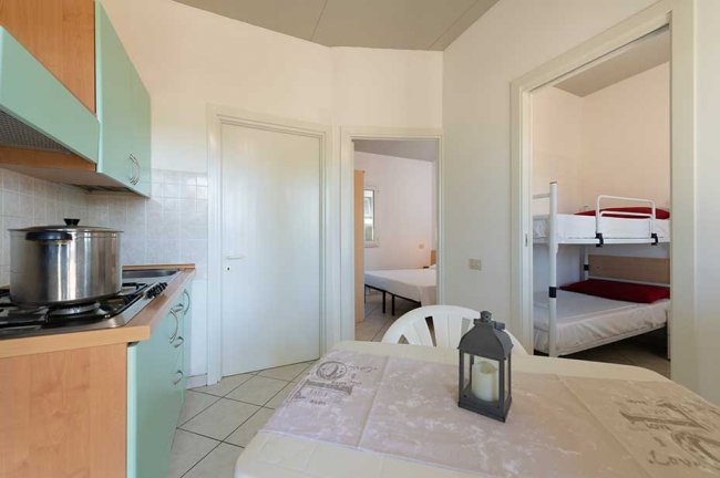 Interno di una cucina con tavolo, stoviglie, e porte verso le camere da letto.