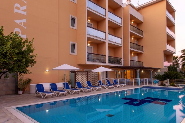 Piscina di fronte a un edificio color pesca con lettini e ombrelloni.
