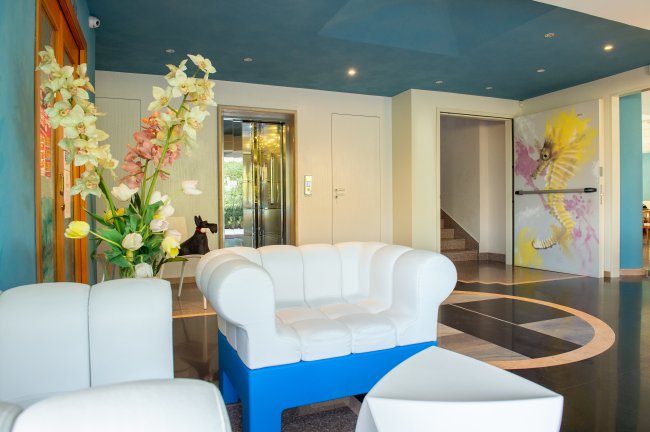 Sala d'attesa moderna con divani bianchi e grandi fiori decorativi.