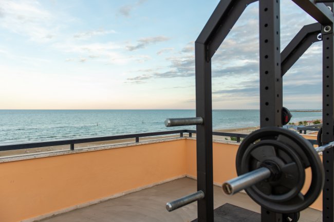 Vista del mare da una terrazza con attrezzature da palestra, inclusi pesi e bilancieri.