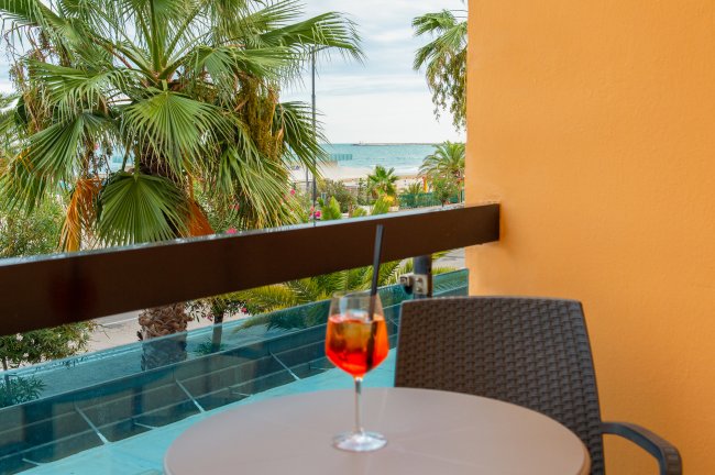 Un tavolino con una bibita arancione, vista su palme e mare.