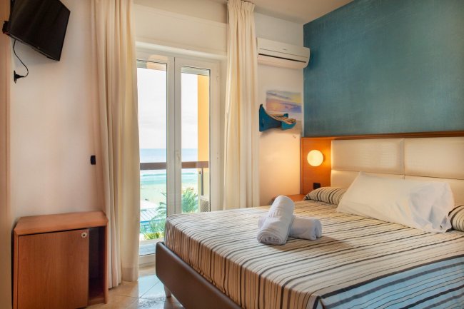 Camera con letto, tende bianche, vista mare.