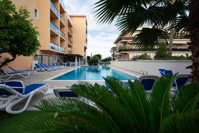 Piscina con lettini blu e palme attorno.