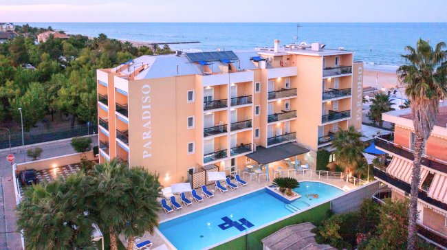 Hotel con piscina vista mare, palme e balconi.