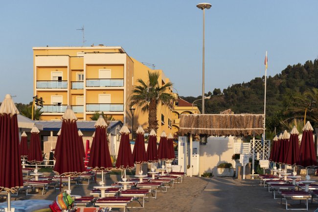 Ombrelloni chiusi su una spiaggia sabbiosa, edificio giallo sullo sfondo.