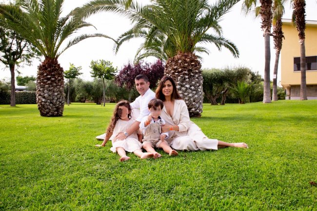 Famiglia seduta su un prato verde, circondata da palme.