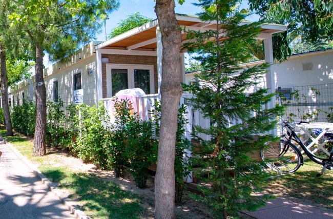 Esterno di un bungalow con veranda, immerso nel verde con bicicletta parcheggiata di lato.