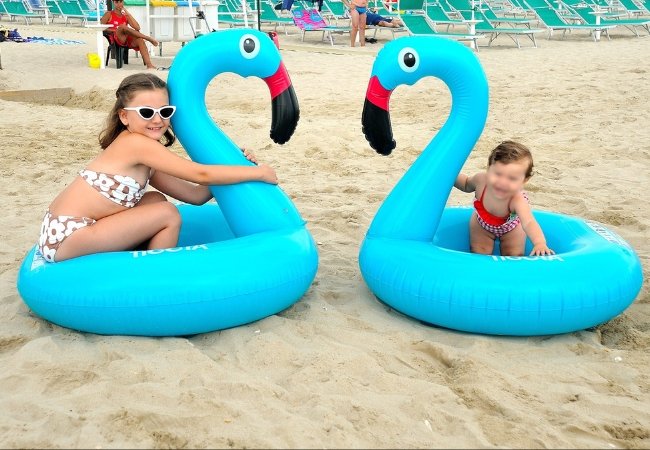 Due bambine giocano sulla spiaggia con gonfiabili a forma di fenicottero blu.