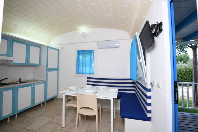 Cucina con tavolo apparecchiato, sedie e panca a righe blu e bianche, accanto a una finestra.