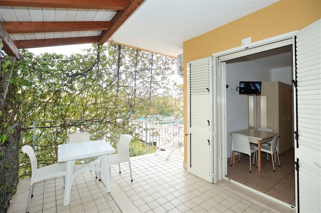 Veranda con tavolo e sedie bianche all'aperto, vista su giardino e ingresso alla stanza.