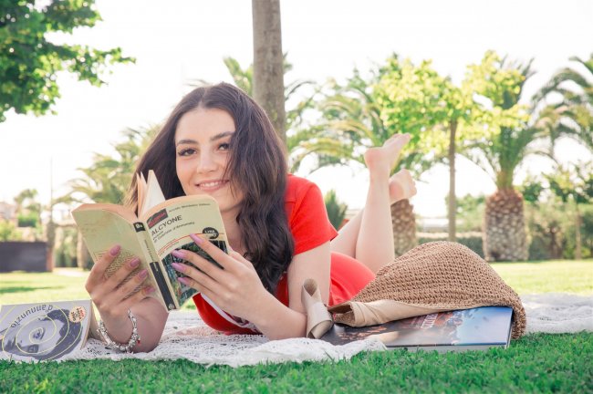 Persona distesa sull'erba che legge un libro. Sfondo con palme.