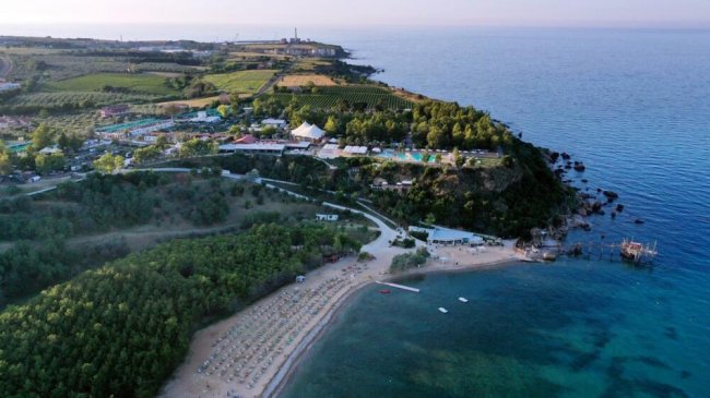 Vista aerea di una spiaggia, mare e vegetazione densa nelle vicinanze.