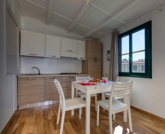 Cucina moderna con tavolo bianco e sedie di legno, pavimento in legno e ampia finestra.