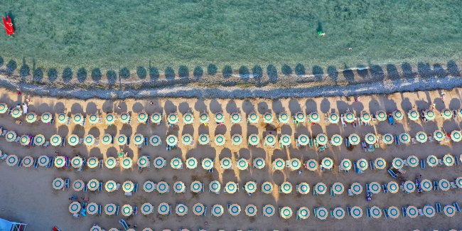 Vista aerea di una spiaggia con molti ombrelloni colorati allineati lungo la riva.