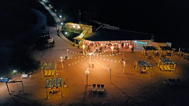 Veduta notturna di una spiaggia illuminata con tavoli coperti e sentiero.