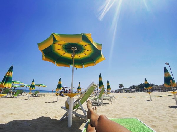 Spiaggia con ombrelloni giallo-verdi sotto un cielo azzurro.