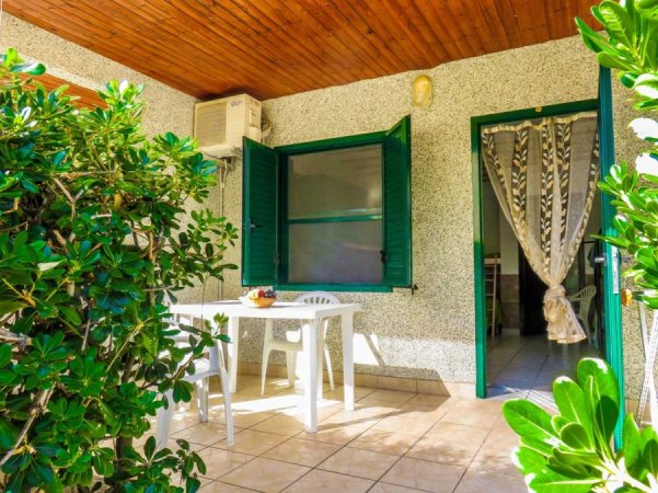 Terrazza con tavolo bianco e sedie, circondata da piante verdi e ingresso con porta a tende.