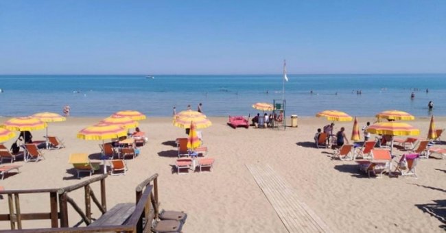 Spiaggia sabbiosa con ombrelloni gialli e arancioni, bagnanti in mare.