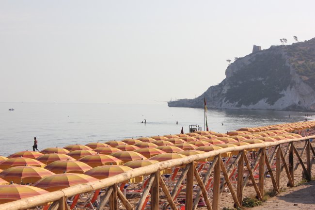 Spiaggia con ombrelloni colorati, scogliera sullo sfondo.