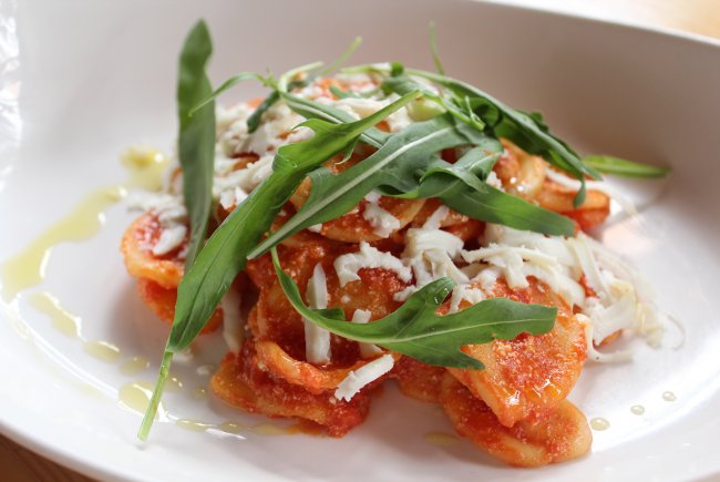 Ravioli al pomodoro con rucola e formaggio grattugiato, su un piatto bianco.