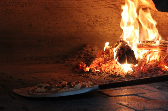 Pizza in un forno a legna, con fiamme visibili.
