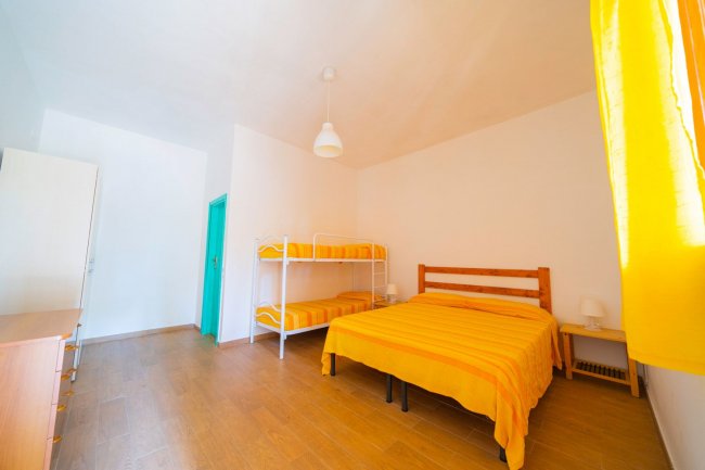 Camera luminosa con letto matrimoniale e letto a castello, tende gialle.