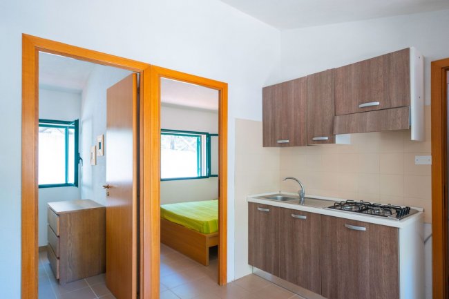 Un angolo cottura con mobili in legno e due porte aperte che conducono a una stanza con letto.