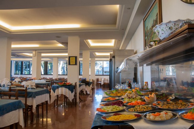 Sala da pranzo elegante con tavoli apparecchiati e buffet ricco di piatti colorati.