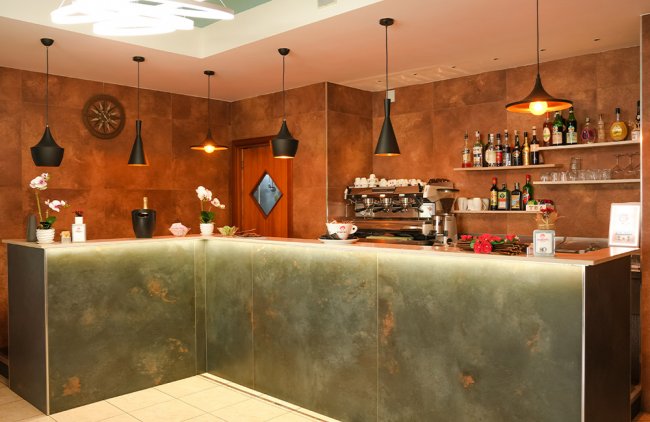 Bar con bancone moderno, luci pendenti nere e scaffali di bottiglie.