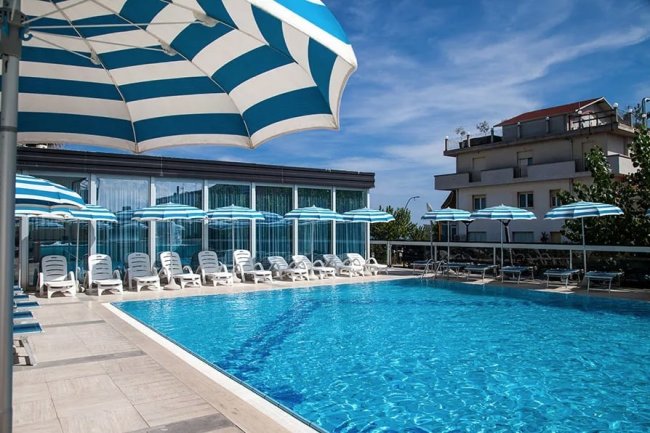 Piscina all'aperto con lettini e ombrelloni blu e bianchi.
