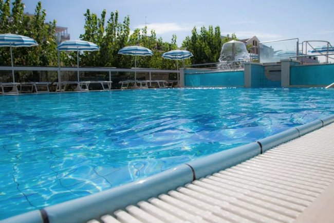 Piscina azzurra all'aperto con ombrelloni e lettini sullo sfondo.
