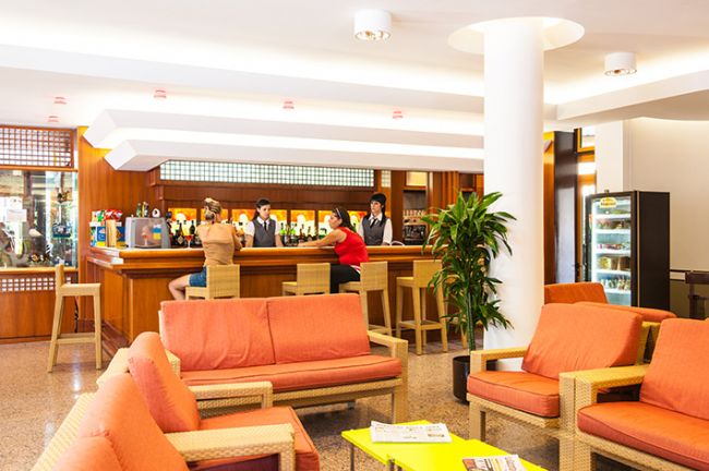 Lounge bar con divani arancioni, tre persone al bancone, pianta decorativa.