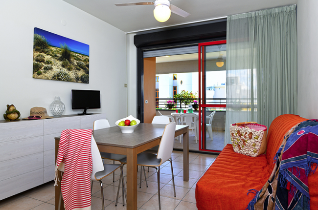 Interno di un soggiorno con tavolo da pranzo, divano arancione e balcone.