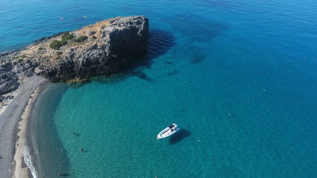 Vista aerea di una barca bianca vicino a una scogliera e una spiaggia con acque cristalline.