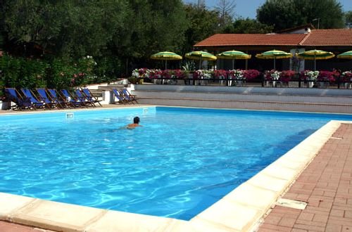 Piscina con un nuotatore e file di lettini blu, ombrelloni e fiori di sfondo.