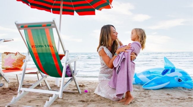 Donna con bambina sulla spiaggia sotto ombrellone colorato.