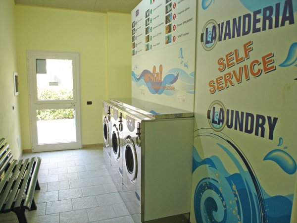 Interno di una lavanderia self-service con lavatrici e panchina.